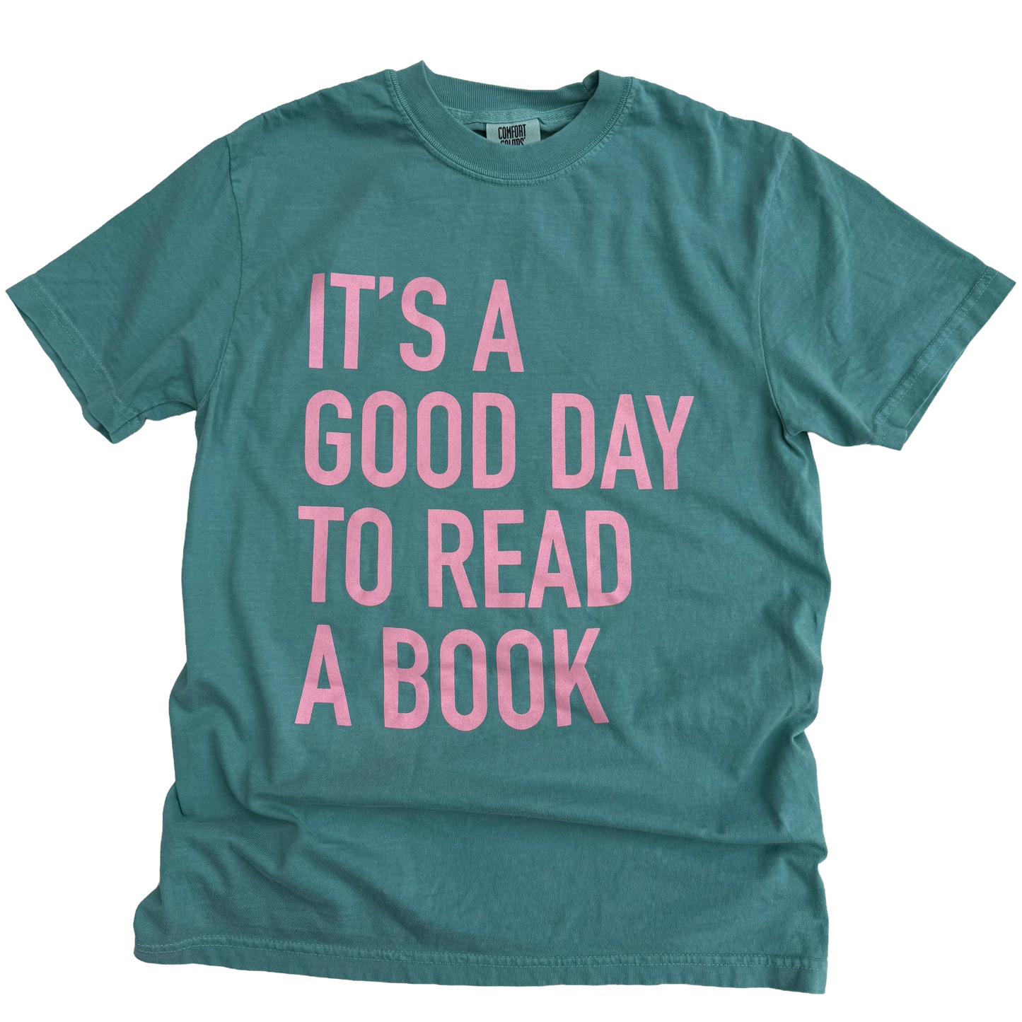 Teal t-shirt with pink text 'It's a good day to read a book' on a white background