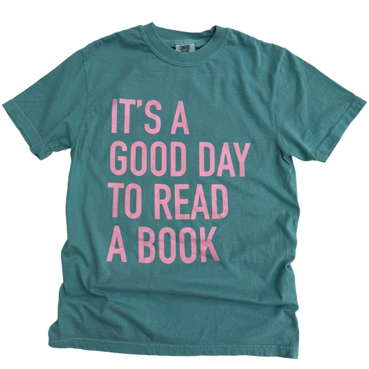 Teal t-shirt with pink text 'It's a good day to read a book' on a white background