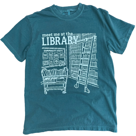 Teal t-shirt with white library graphic and text 'meet me at the LIBRARY'.